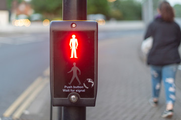 push button wait for signal traffic light control with bright stop man illuminated at pedestrian crossing and woman walking past