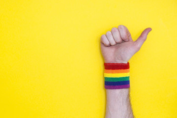 Thumbs up hand with gay pride rainbow flag wristband on a yellow background