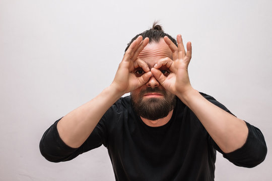 A Man With A Beard In A Black T-shirt Shows His Fingers That He Is Looking Through Binoculars