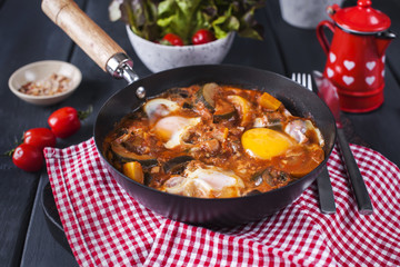 Traditional Mexican dish Huevos rancheros - scrambled eggs with tomato salsa, with taco tortillas, fresh vegetables and parsley. Breakfast. On a black concrete table. With a forks, copy space