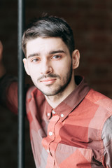 Fototapeta premium Charismatic young man at a photo shoot in the interior loft Studio. Sitting on floor and looking at the camera. Casual look and plaid shirt