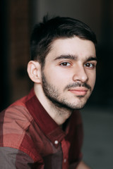 Fototapeta premium Charismatic young man at a photo shoot in the interior loft Studio. Sitting on floor and looking at the camera. Casual look and plaid shirt