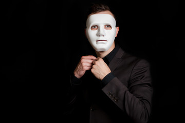 A man on a black background in a white mask. Button a button on his shirt