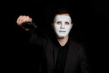 Man on a black background in a white mask. Threatens with a pistol. - obrazy, fototapety, plakaty