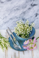 Spring Table Setting with Vintage Blue Cutlery , Lily of the Valley Flowers and Pink Tulip  on a Marble Background.Floral Table Decor