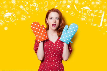 Surprised redhead girl in red polka dot dress and mittens and drawn kitchenware on yellow background. - obrazy, fototapety, plakaty