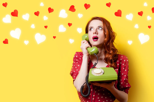 Surprised redhead girl in red polka dot dress with green dial phone and hearts on yellow background.