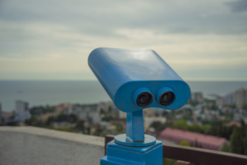 blue binoculars on the observation deck on the background of the city and the sea