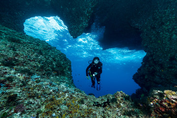 woman diver underwater at the entrance of a cave with sunrays