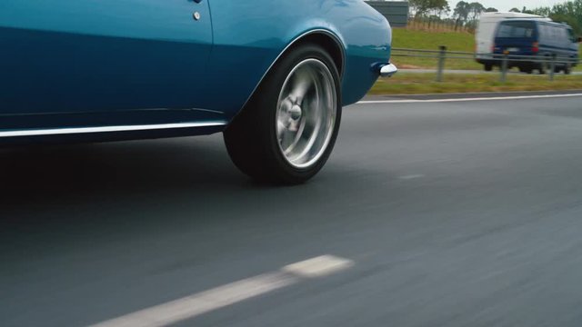 Back wheel of blue car driving down road