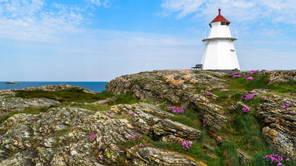 The Krogsta lighthouse in rocky coastal landscape on a sunny morning. An empty bench is visible beside the lighthouse.