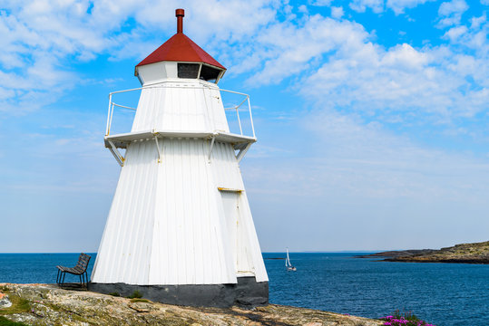 The Krogsta lighthouse in rocky coastal landscape on a sunny morning. An empty bench is visible beside the lighthouse.