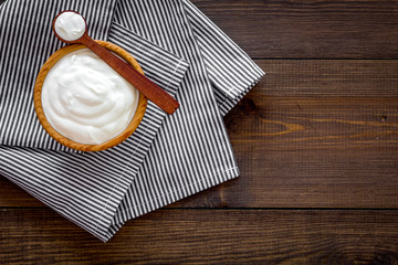 Food helps digestion. Greek yogurt in brown bowl near spoon on blue tablecloth, dark wooden background top view copy space