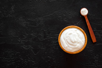 Healthy product, healthy meal. Greek yogurt in brown bowl near spoon on black background top view copy space