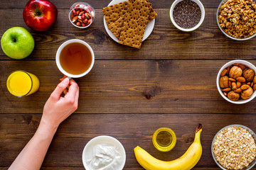 Set of products for healthy vegetarian breakfast. Fruits, oatmeal, yogurt, nuts, crispbreads, chia on dark wooden background top view space for text. Hand takes tea
