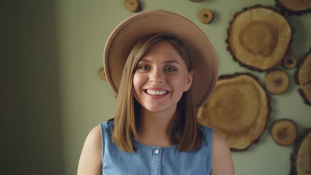Slow motion of pretty blond girl in trendy hat and denim top looking at camera, smiling and laughing. Attractive people and positive emotions concept.