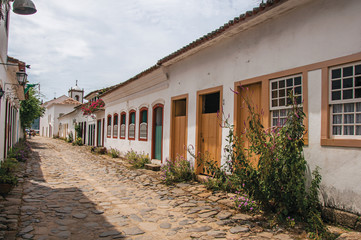 Fototapeta na wymiar View of cobblestone alley with old colorful houses and blue cloudy sky in Paraty, an amazing and historic town totally preserved in the coast of the Rio de Janeiro State, southwestern Brazil 