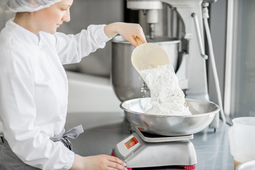 Woman confectioner in uniform weighing ingredients for pastry working at the bakery manufacturing