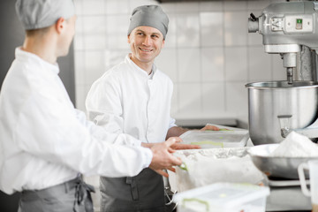 Two male confectioners preparing ingredients for baking standing at the manufacturing