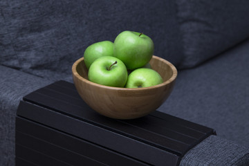 green fresh apples are in a wooden bowl in the kitchen