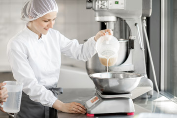 Woman confectioner in uniform weighing ingredients for pastry working at the bakery manufacturing