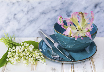 Spring Table Setting with Vintage Blue Cutlery , Lily of the Valley Flowers and Pink Tulip  on a Marble Background.Floral Table Decor