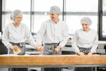 Three bakers having fun forming dough for baking standing together at the modern manufacturing