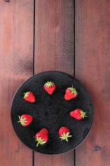 Obraz na płótnie Canvas Strawberries on a black plate top view, red berries on a wooden background, fresh strawberries on dark wooden boards, vegetarian food