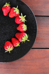Strawberries on a black plate top view, red berries on a wooden background, fresh strawberries on dark wooden boards, vegetarian food