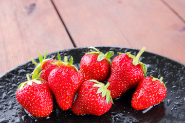 Strawberries on a black plate top view, red berries on a wooden background, fresh strawberries on dark wooden boards, vegetarian food