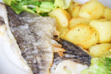 homemade dinner on a white plate baked potatoes fried fish cod, green lettuce with spices,
