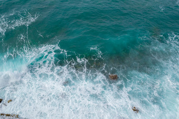 Fototapeta premium Big waves breaking on the shore. Waves and white foam. Coastal stones. View from above. The marine background is green