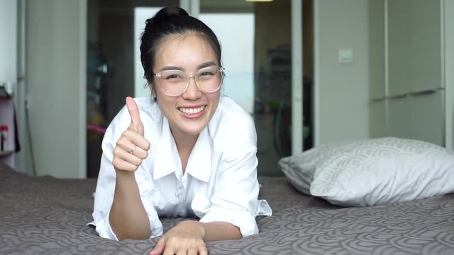 Beautiful Asian woman laughing shows Thumbs up on bed. attractive girl looking at the camera smiling 