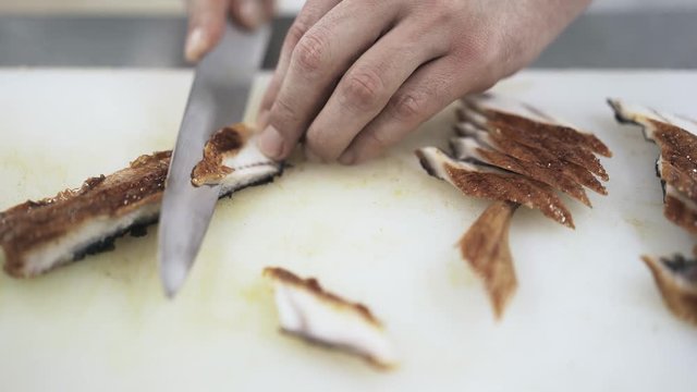 Hands of an unrecognizable cook cutting fish in slices in a modern restaurant. Making sushi. Japanese culture concept. Locked down real time close up shot