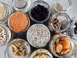 Healthy cereals and fruits in glass jars and reusable bags with fresh basil on wooden background in daylight