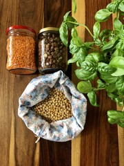 Healthy cereals and fruits in glass jars and reusable bags with fresh basil on wooden background in daylight
