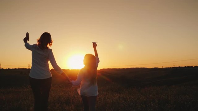 Mom and daughter are playing paper airplanes at sunset. In a picturesque place. Happy time with the baby concept