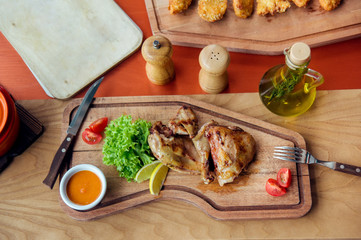 fried chicken parts is on wooden board served with salad, tomatoes, oil and spices