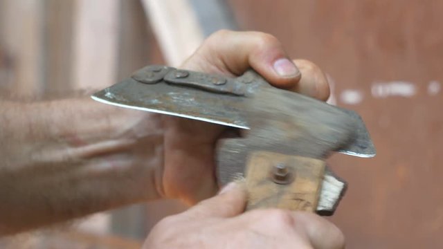 Old man sharpening the hoe. Work on a sharpening machine.