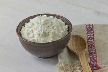 Cottage cheese in a brown ceramic bowl with frozen raspberries and blackberries with authentic flax embroidered napkin and a wooden spoon on a white wooden background.  Close-up.