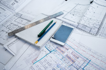 Green pen, blue pencil, white cellphone, metal ruler, notepad and some paper draws of a house (home) are laying down on white table. All staff is for a architecture negotiation.