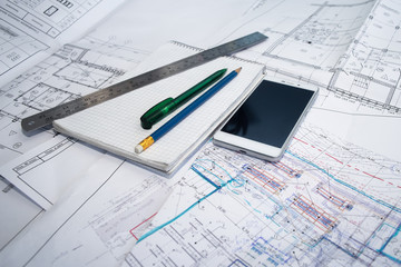 Green pen, blue pencil, white cellphone, metal ruler, notepad and some paper draws of a house (home) are laying down on white table. All staff is for a architecture negotiation.