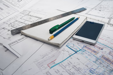 Green pen, blue pencil, white cellphone, metal ruler, notepad and some paper draws of a house (home) are laying down on white table. All staff is for a architecture negotiation.