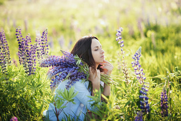 Beautiful girl in blue dress holding a lupine at sunset on the field. The concept of nature and romance
