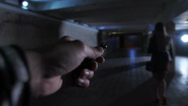 Attacker point of view shot. Male attacker's hand with knife following young woman walking at dark underpass tunnel alone at night. Criminal killer chasing his victim at darkness