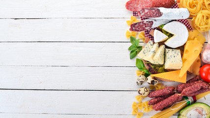 Assortment of sausage, cheese and fresh vegetables. On a white wooden background. Top view. Copy space.