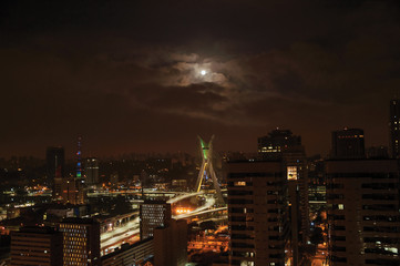 Night view of the city skyline with bridge and buildings under cloudy and full moon in the city of São Paulo. The gigantic city, famous for its cultural and business vocation.