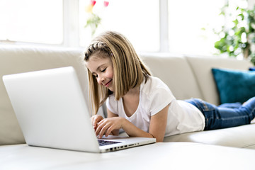 Happy little girl at home working with a laptop on sofa