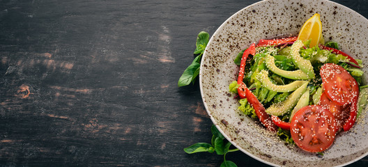 Salad with avocado, tomato and fresh vegetables. On a wooden background. Top view. Copy space.