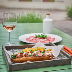 sandwich with baguette and meat on a background of a green table and a glass of pink wine and prosciutto. italian fast food